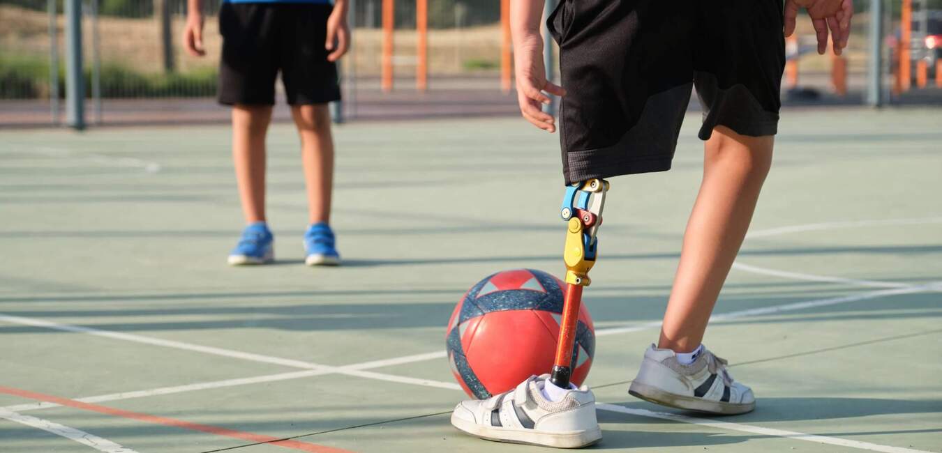 Nahaufnahme eines Jungen mit Prothesenbeinum, der einen Fußball auf einem Sportplatz dribbelt.