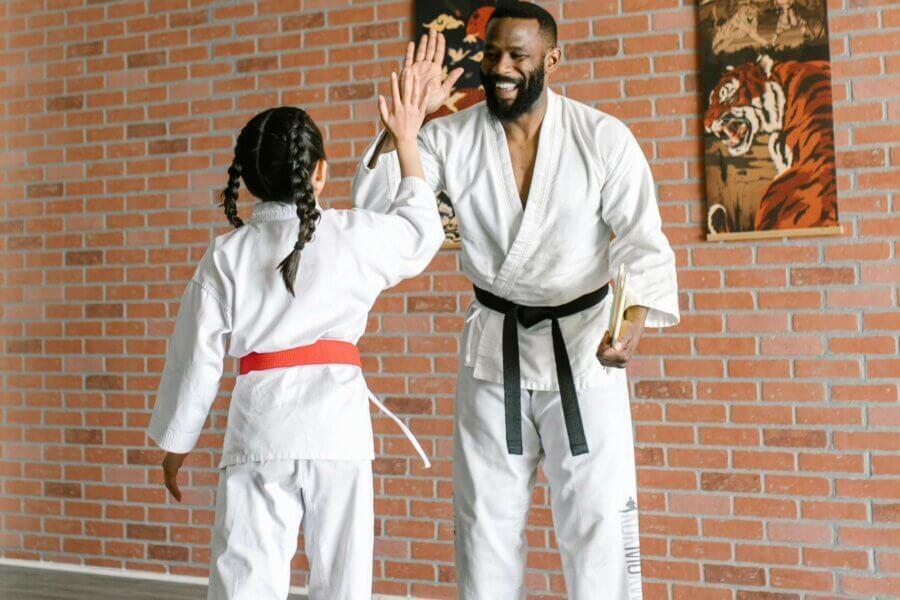 Junge und Trainer im Karate-Gi geben sich in einem Trainingsraum mit Ziegelwand ein High-Five.