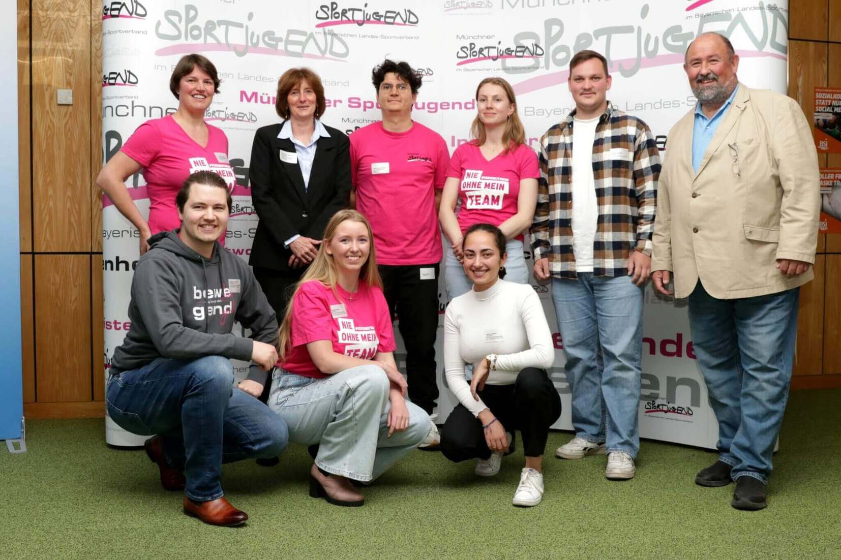 Gruppenfoto von zehn Personen in Freizeitkleidung vor einem Banner, das den Schriftzug „Sportjugend“ zeigt.