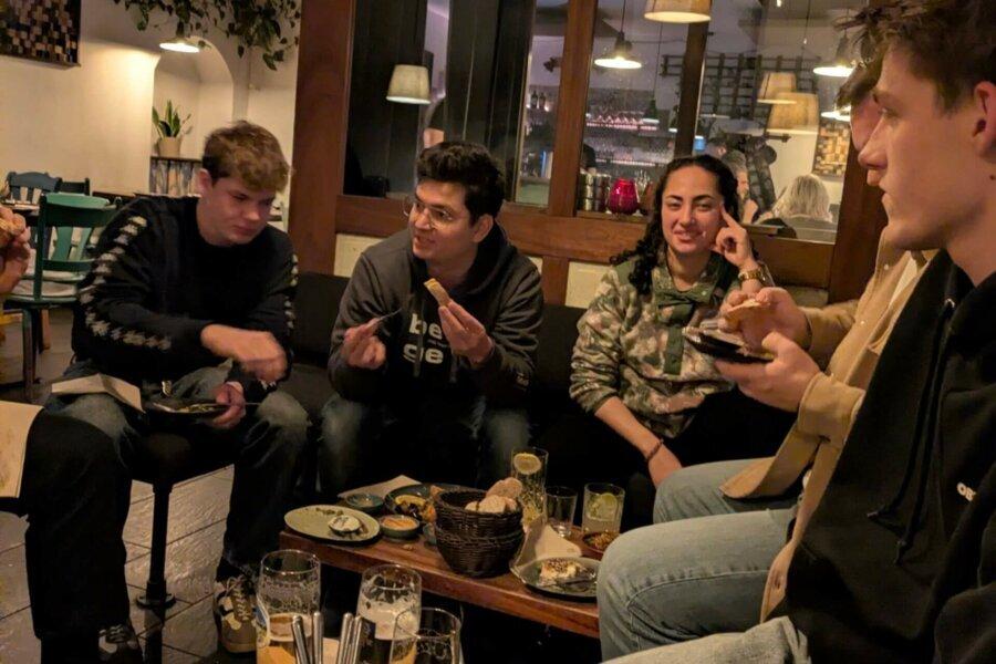 Fünf Personen sitzen in einem Restaurant um einen Tisch mit verschiedenen Speisen und Getränken.