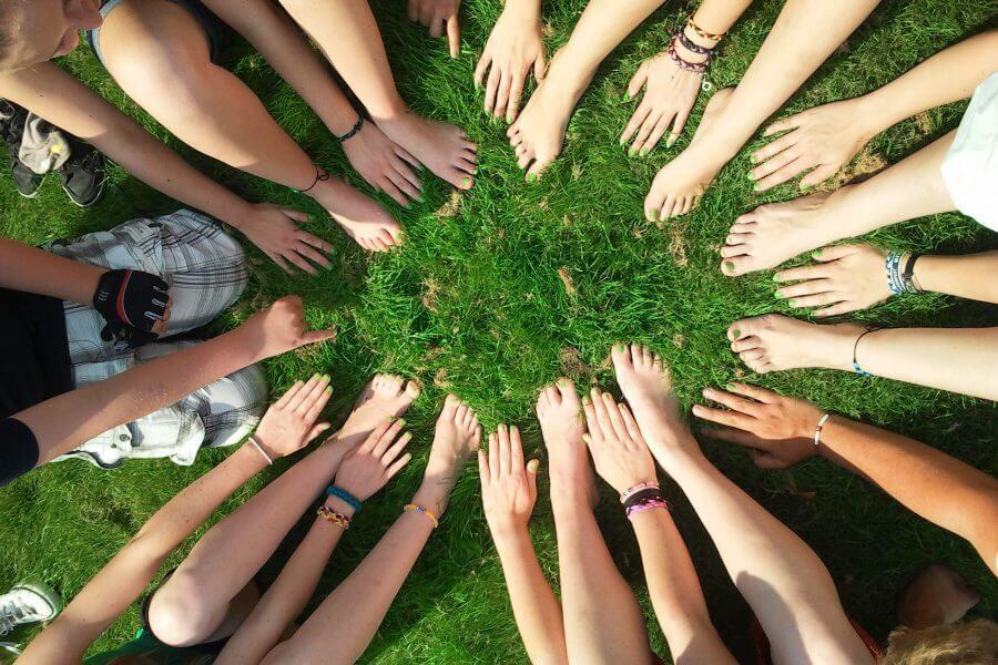 Kreise von Händen und Füßen, die auf grünem Gras angeordnet sind, symbolisieren Gemeinschaft und Zusammenarbeit.