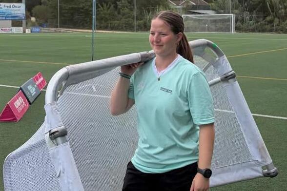 Junge Frau im Fußballoutfit trägt kleines Fußballtor