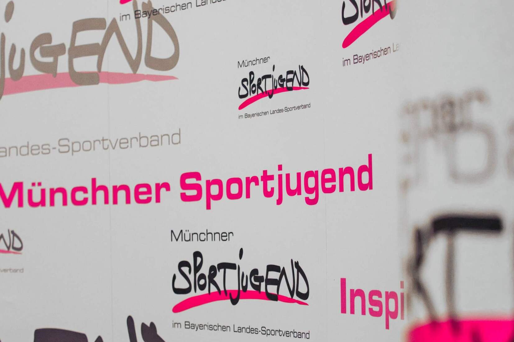 Hintergrund mit verschiedenen Logos und Schriftzügen der Münchner Sportjugend in unterschiedlichen Farben und Schriftarten.