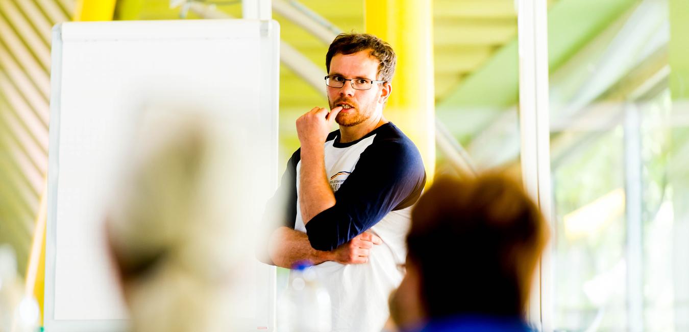 Mann mit Brille spricht vor einer Gruppe, ein Flipchart ist im Hintergrund sichtbar.